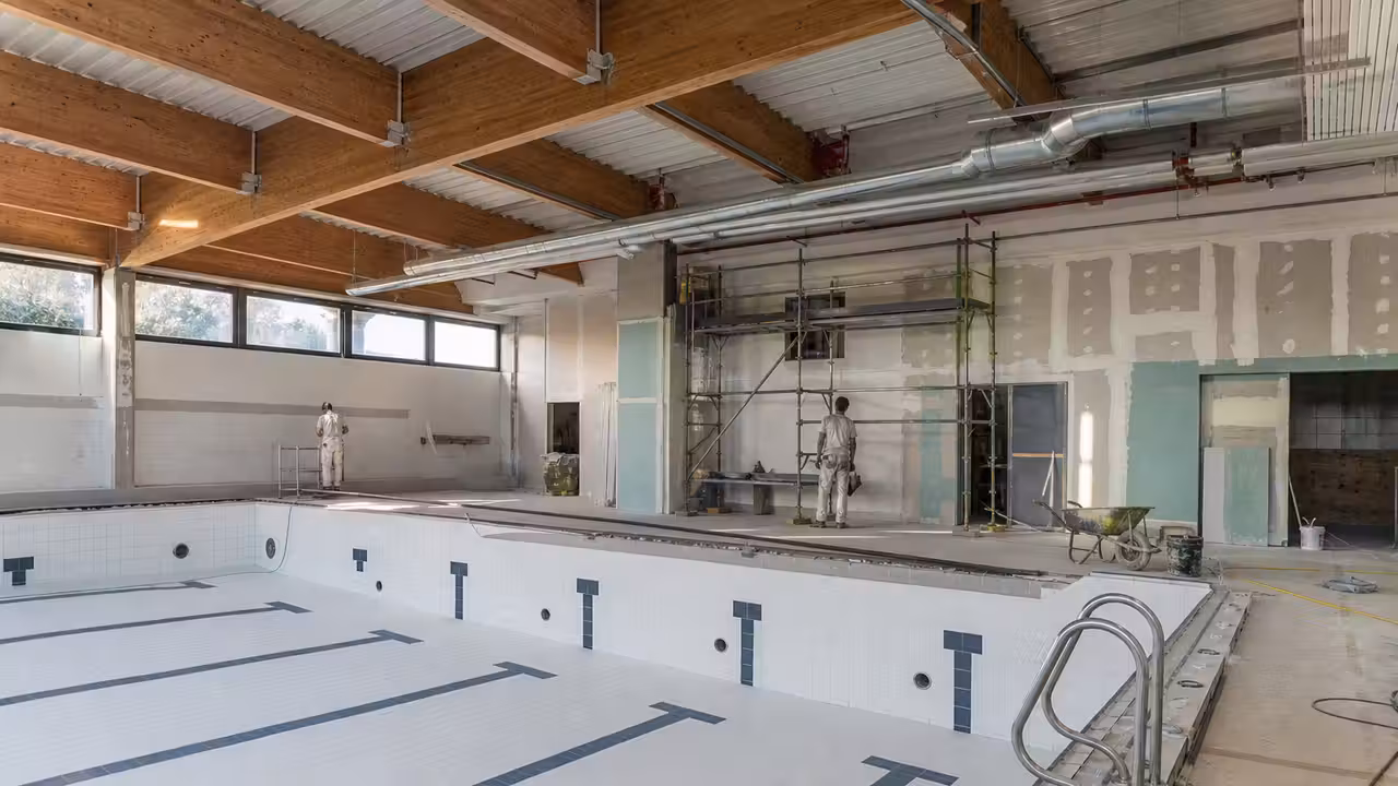 Bassin couvert municipal en rénovation, avec échafaudages et réseaux techniques apparents au plafond