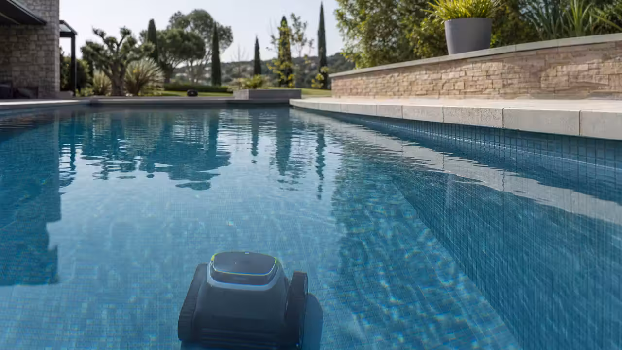 Robot nettoyeur sans fil progressant au fond d’une piscine privée, près d’une paroi immergée.