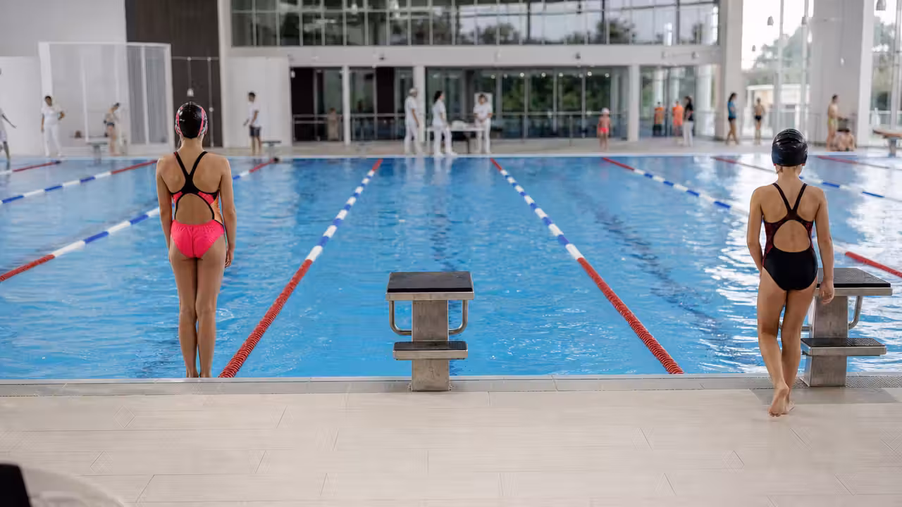 Jeunes nageurs alignés au bord d’un bassin municipal avant le départ d’une compétition de natation.