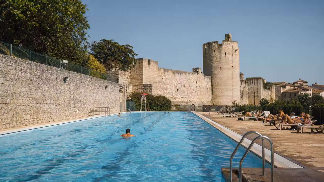 Bassin extérieur de 25 mètres au pied de remparts, avec nageurs et espace de détente en été