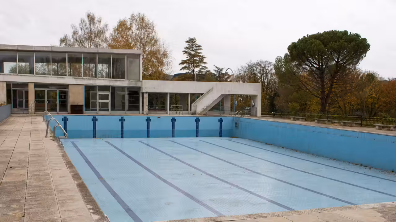 Piscine municipale extérieure des années 1960 avec bassins vides, plages minérales et architecture moderniste