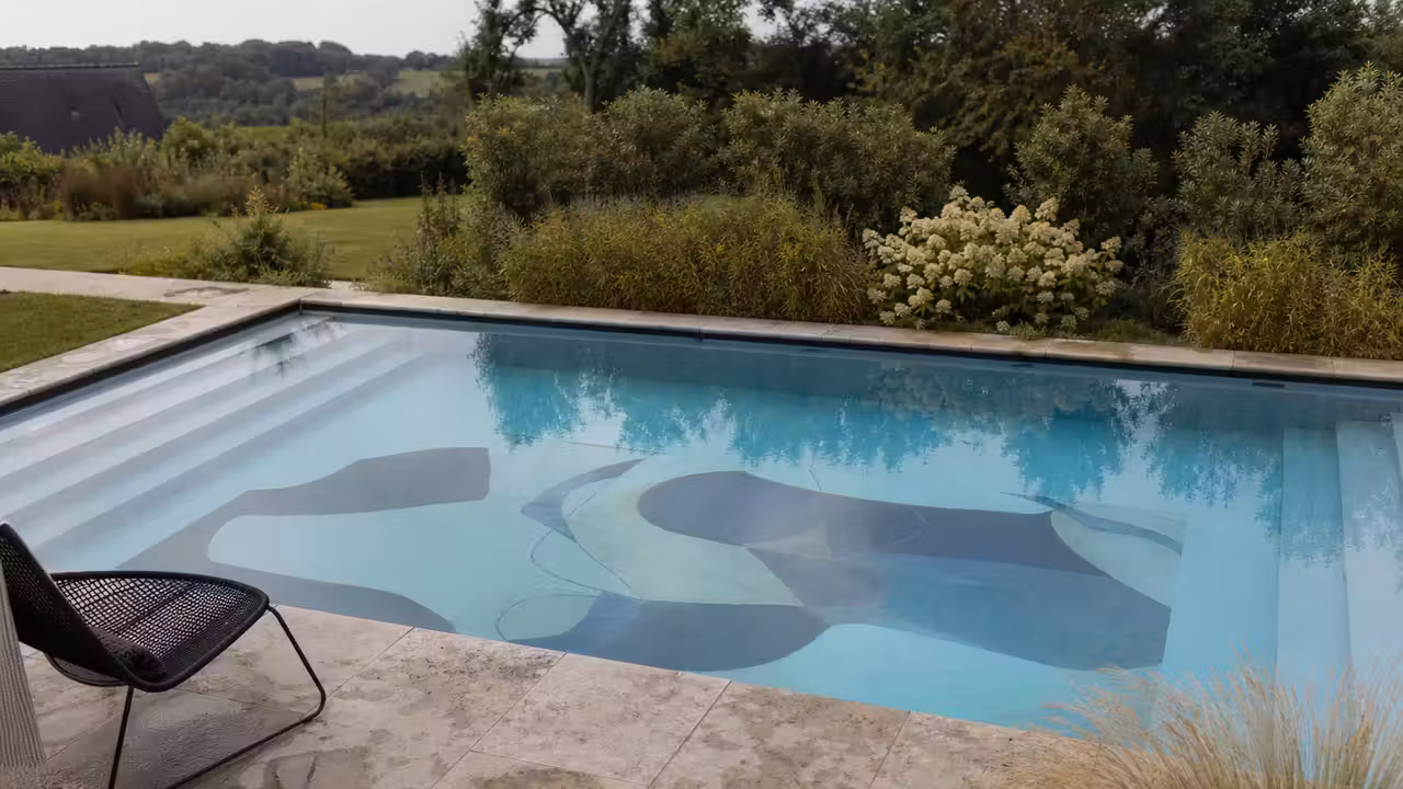 Bassin contemporain semi-enterré avec décor graphique au fond, vu depuis une terrasse paysagée
