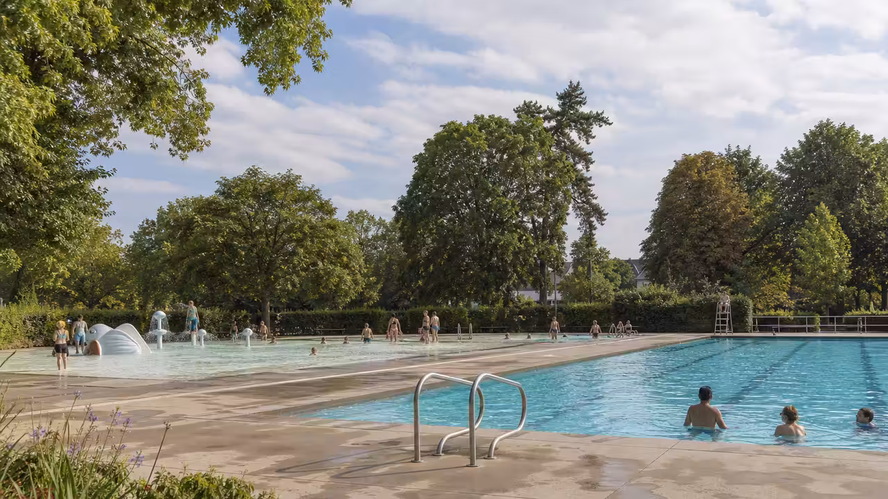 Bassin extérieur entouré d’arbres avec nageurs et zone de détente dans un parc municipal en été