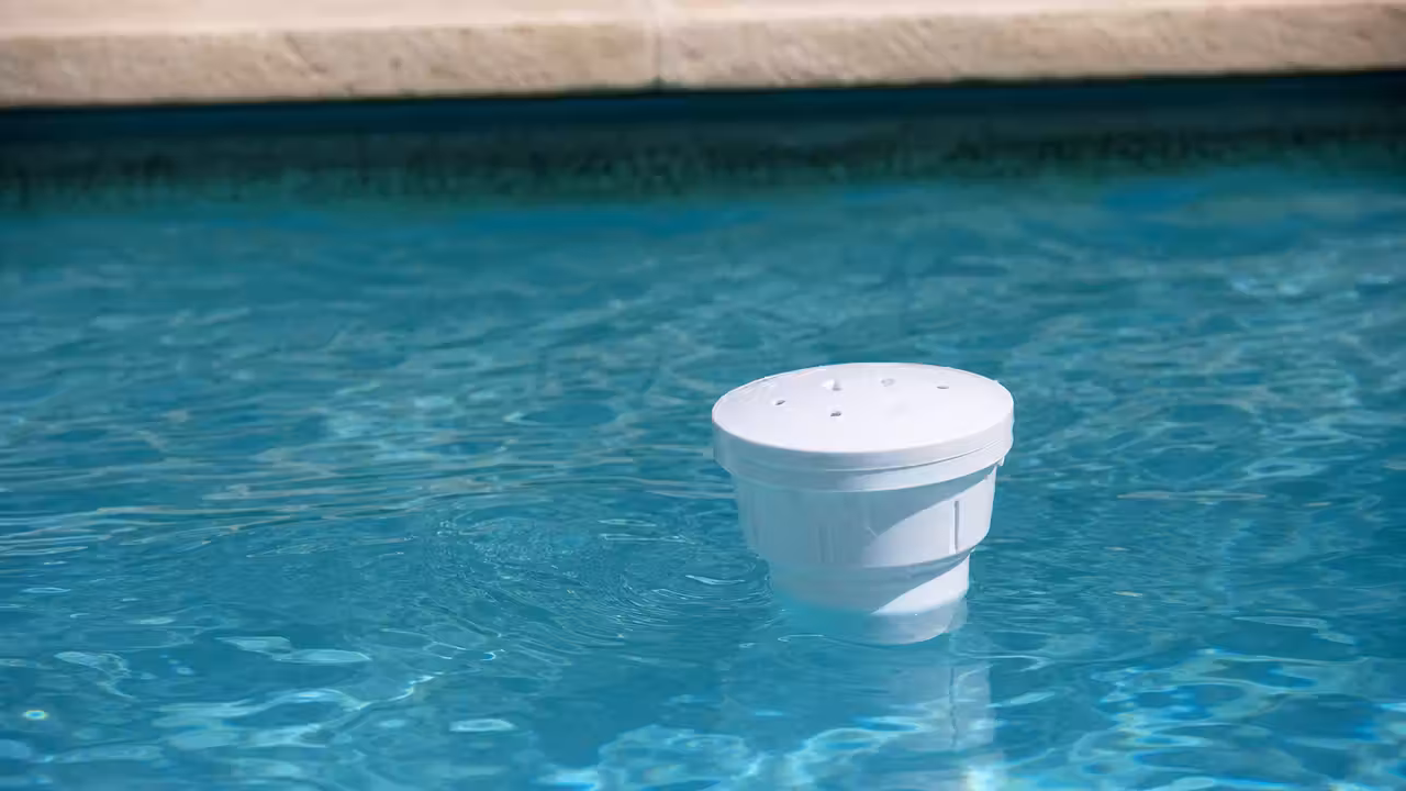 Diffuseur flottant blanc contenant un galet de chlore, dérivant à la surface d'une piscine privée par temps clair