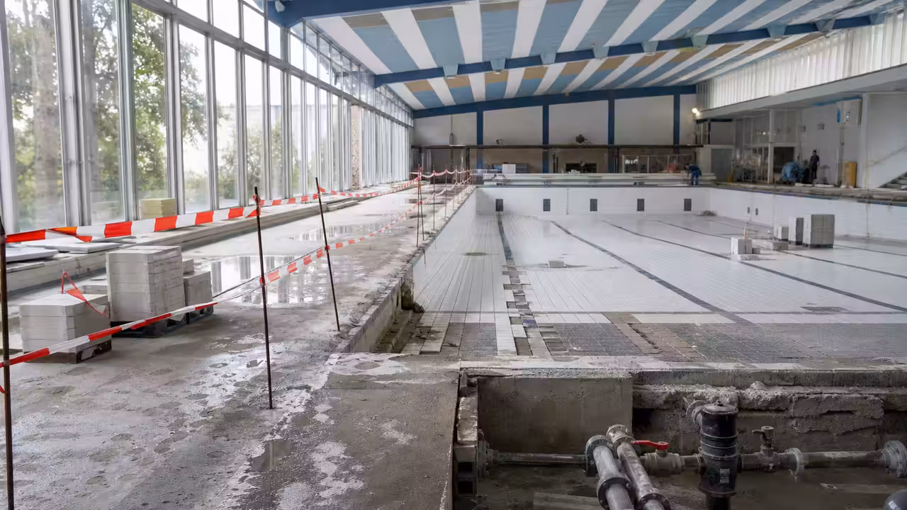 Bassin municipal vide en rénovation, avec couloirs de nage et équipements techniques de chantier en arrière-plan