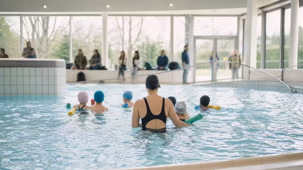 Enfant accompagné par un maître-nageur dans un bassin d’apprentissage d’une piscine publique couverte