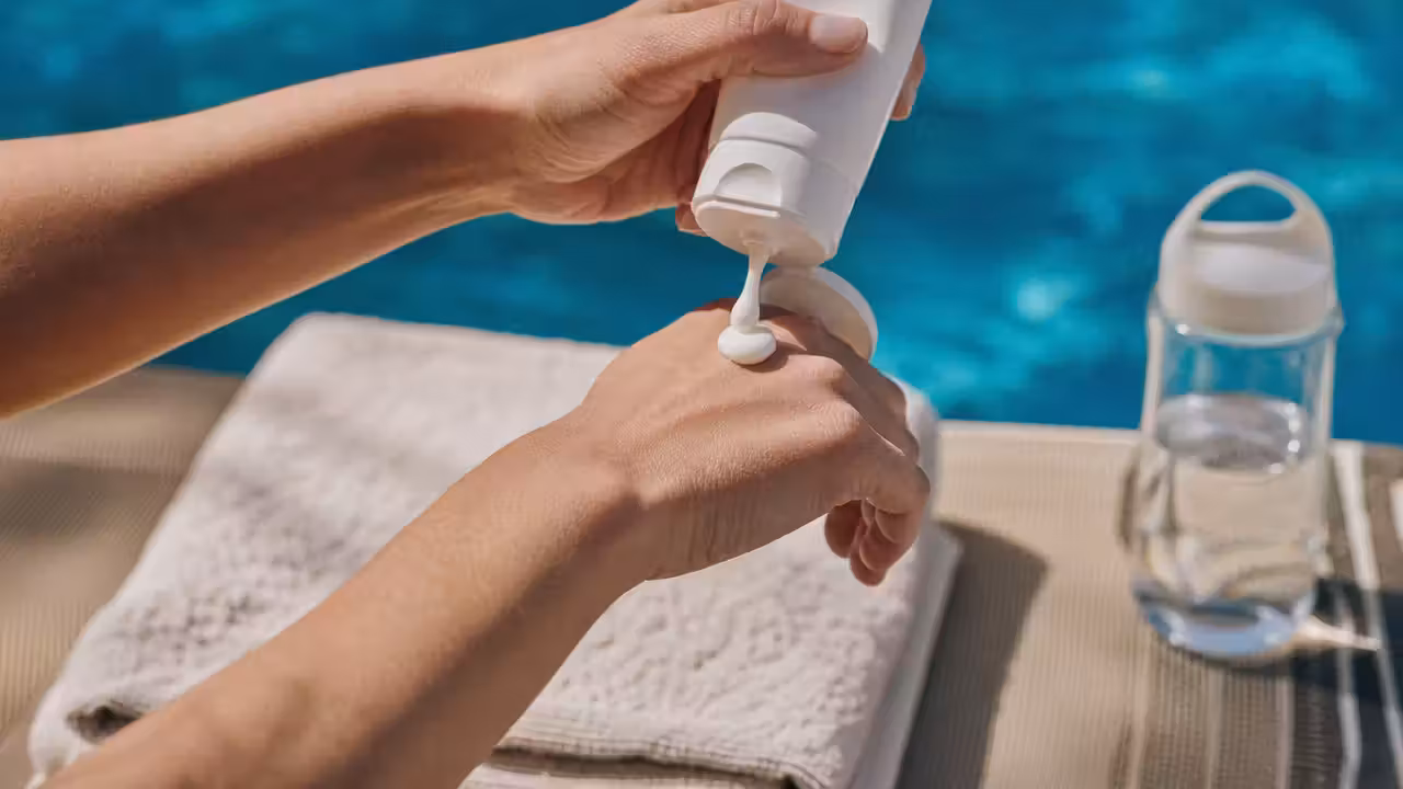 Personne appliquant une crème hydratante sur son avant-bras au bord d'une piscine, peau légèrement sèche