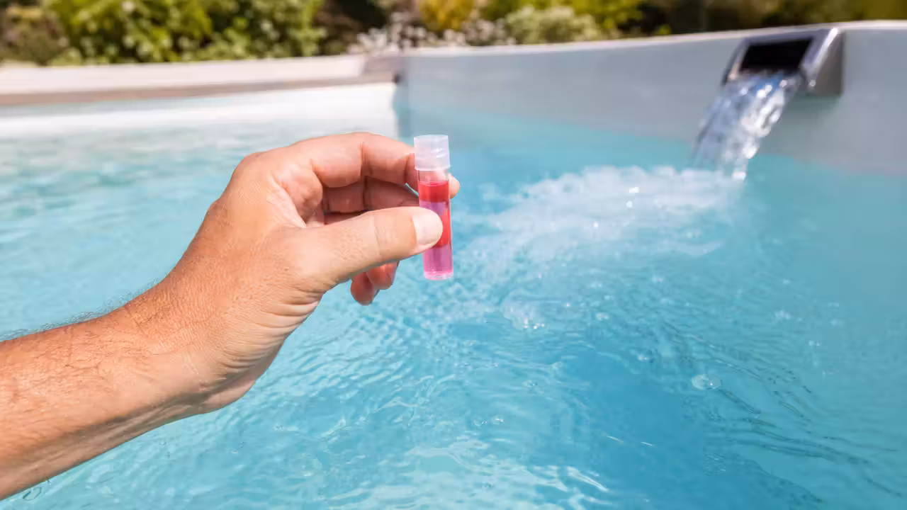 Testeur colorimétrique de pH tenu au-dessus d'une eau de piscine turquoise agitée par un jet
