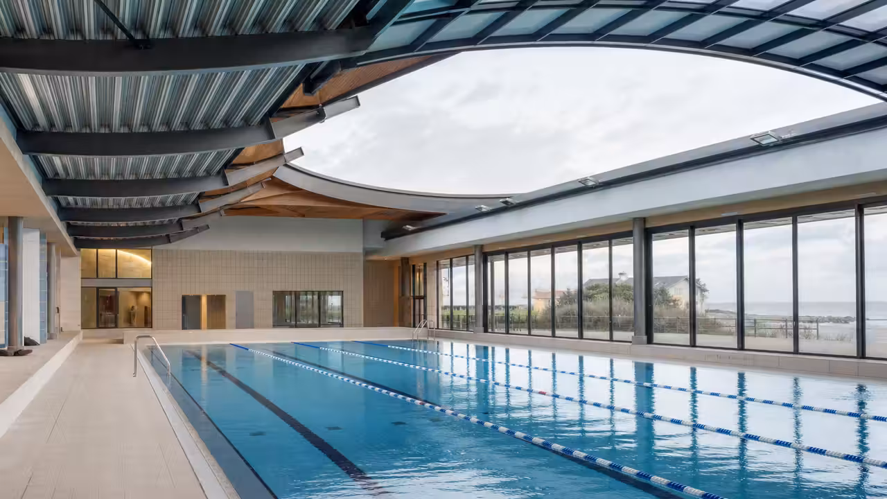 Bassin couvert rénové avec lignes de nage, grandes baies vitrées et plafond technique de piscine publique