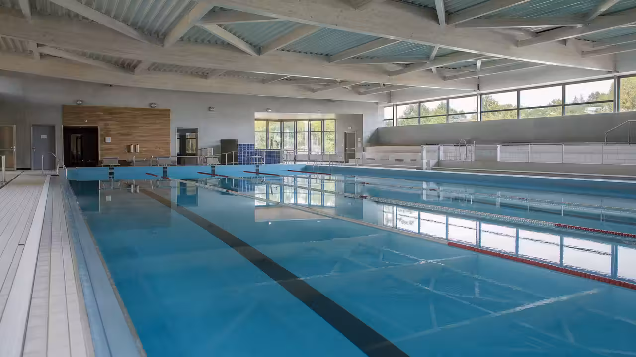 Bassin municipal de 25 mètres rénové, lignes d’eau en place sous une charpente lumineuse
