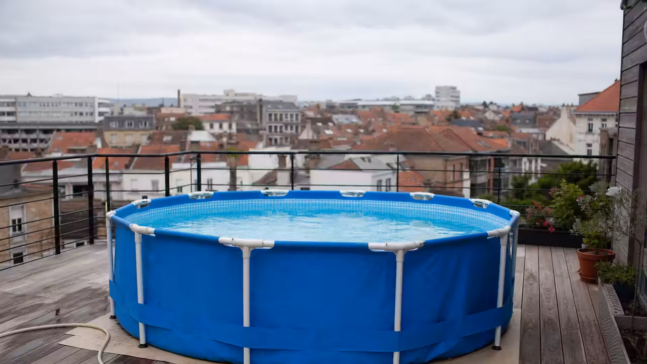 Petite piscine hors-sol tubulaire installée sur une terrasse en bois d’immeuble, garde-corps métallique en arrière-plan