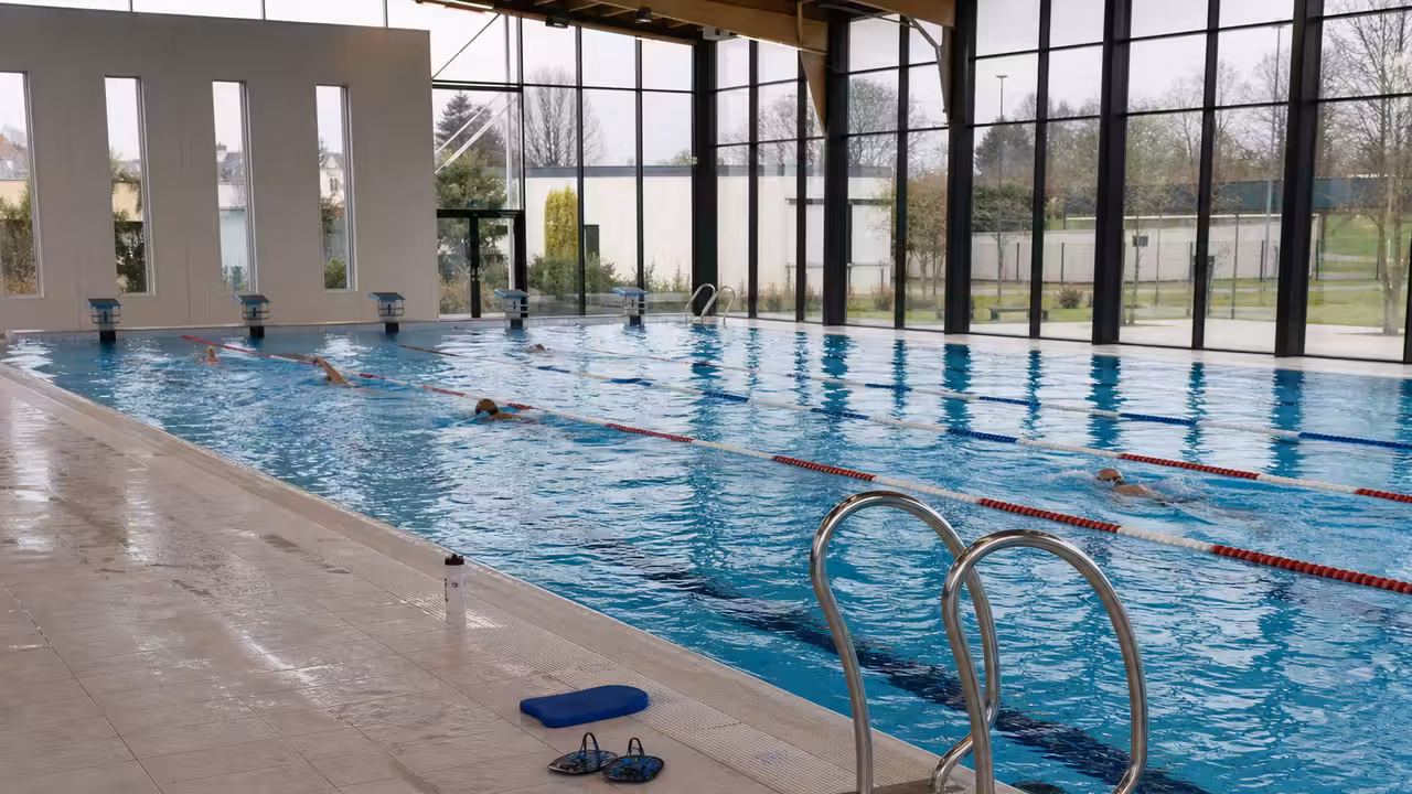 Bassin couvert d’un centre aquatique municipal, avec couloirs de nage et gradins vides en arrière-plan