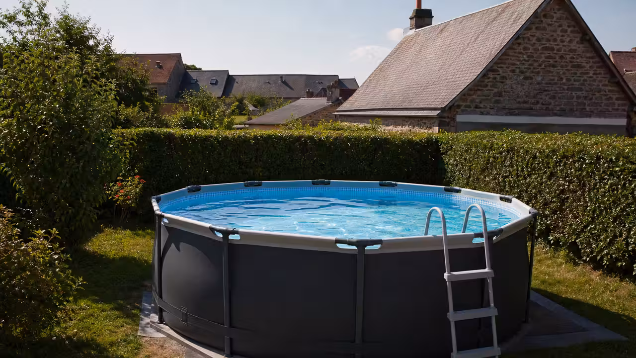 Petite piscine hors-sol tubulaire installée sur la pelouse d'un jardin de maison de ville en fin d'après-midi