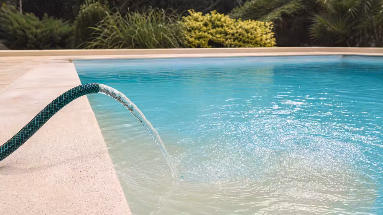 Robinet de remplissage d'une piscine avec de l'eau trouble s'écoulant, bassin en arrière-plan