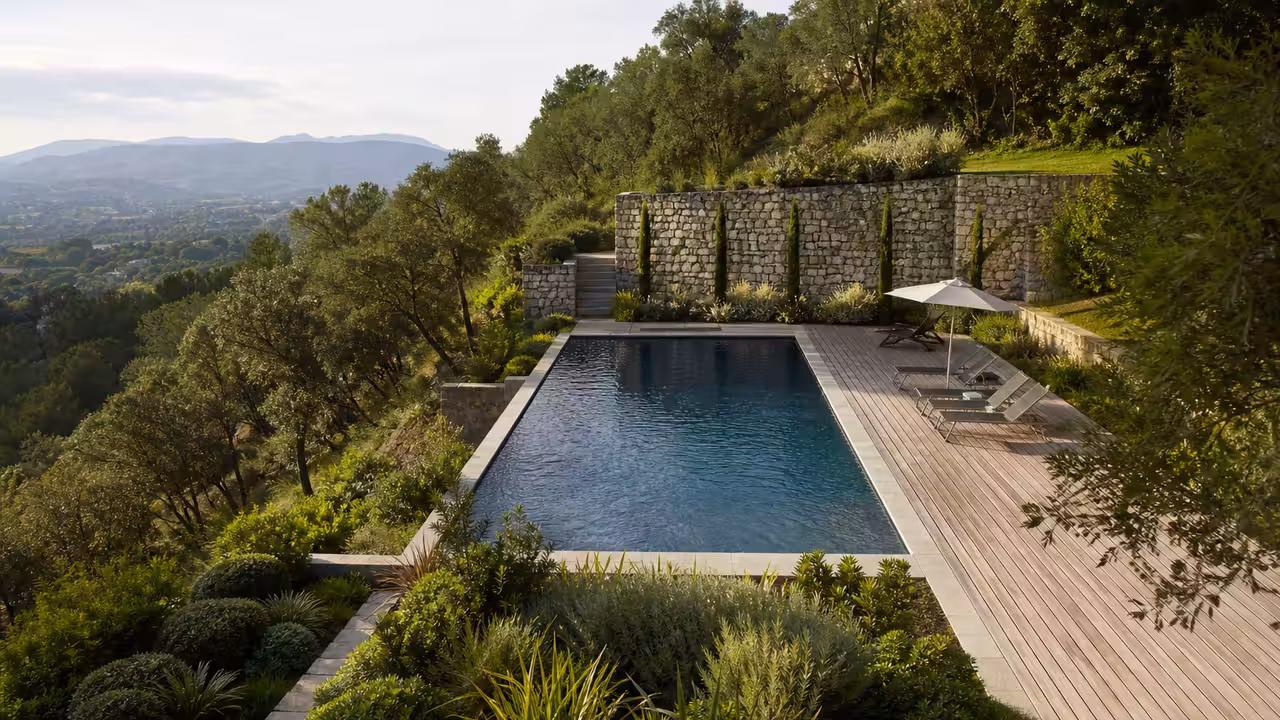 Piscine rectangulaire aménagée dans un jardin en pente, avec mur de soutènement en pierre et terrasses étagées