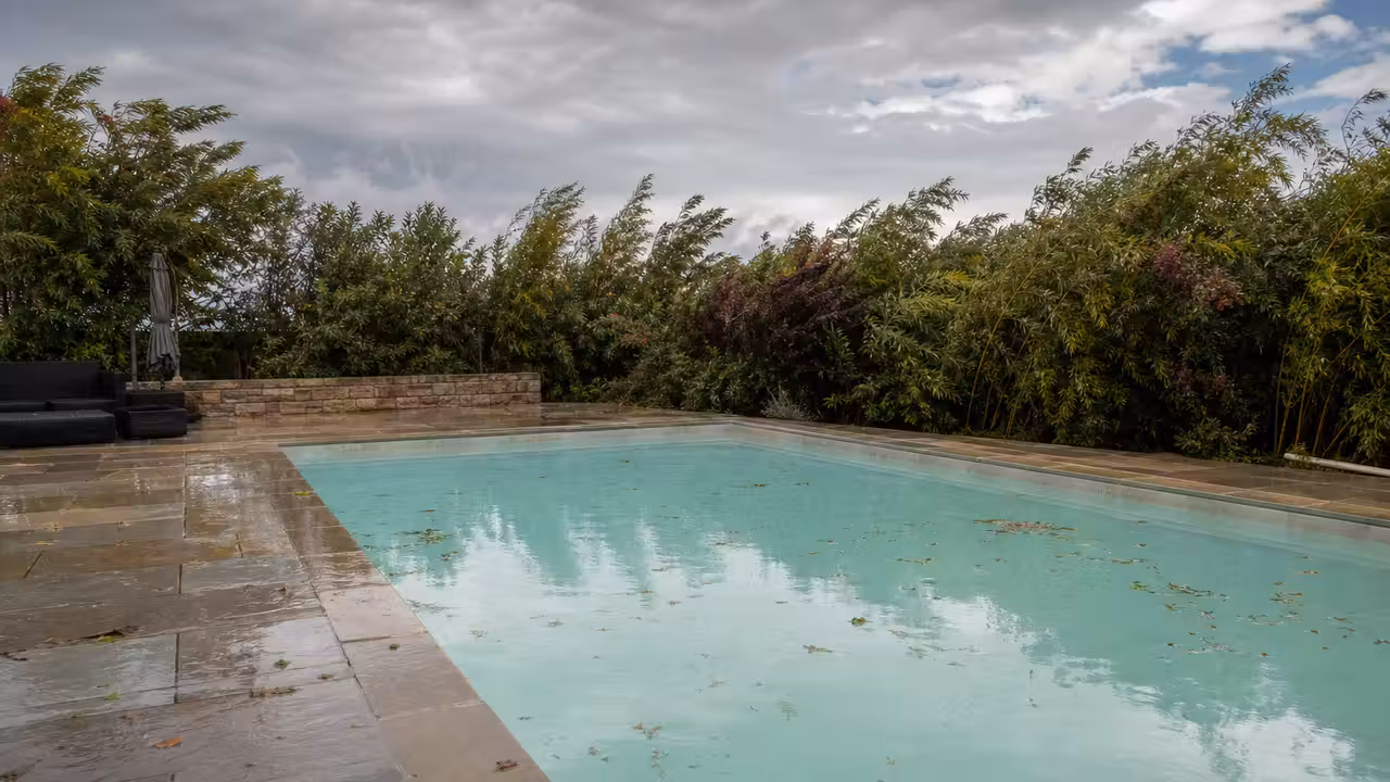Piscine enterrée à l'eau laiteuse au lendemain d'un orage, feuilles et débris flottant près de la margelle mouillée