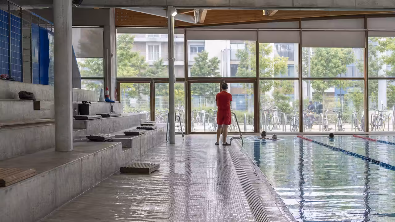 Bassin municipal couvert avec lignes d’eau, grandes baies vitrées et installations techniques discrètes
