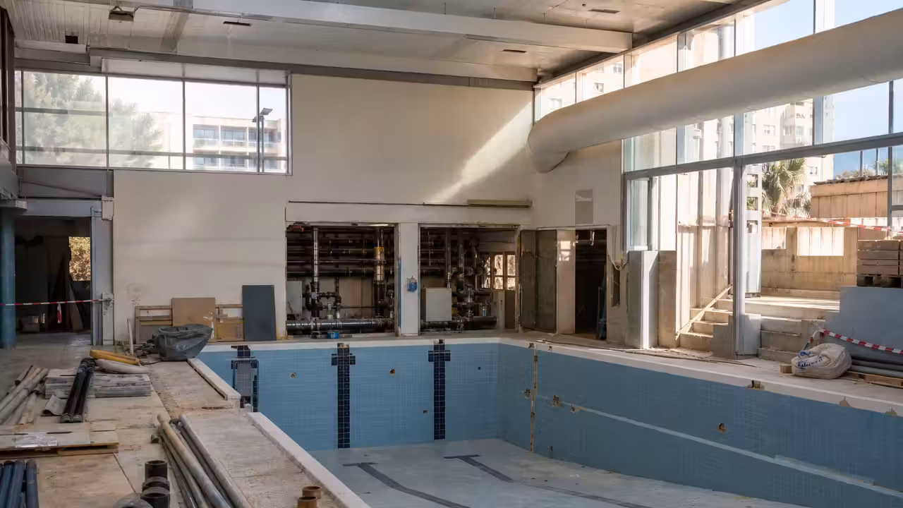 Bassin intérieur vide d’une piscine municipale en rénovation, avec équipements techniques et lumière naturelle