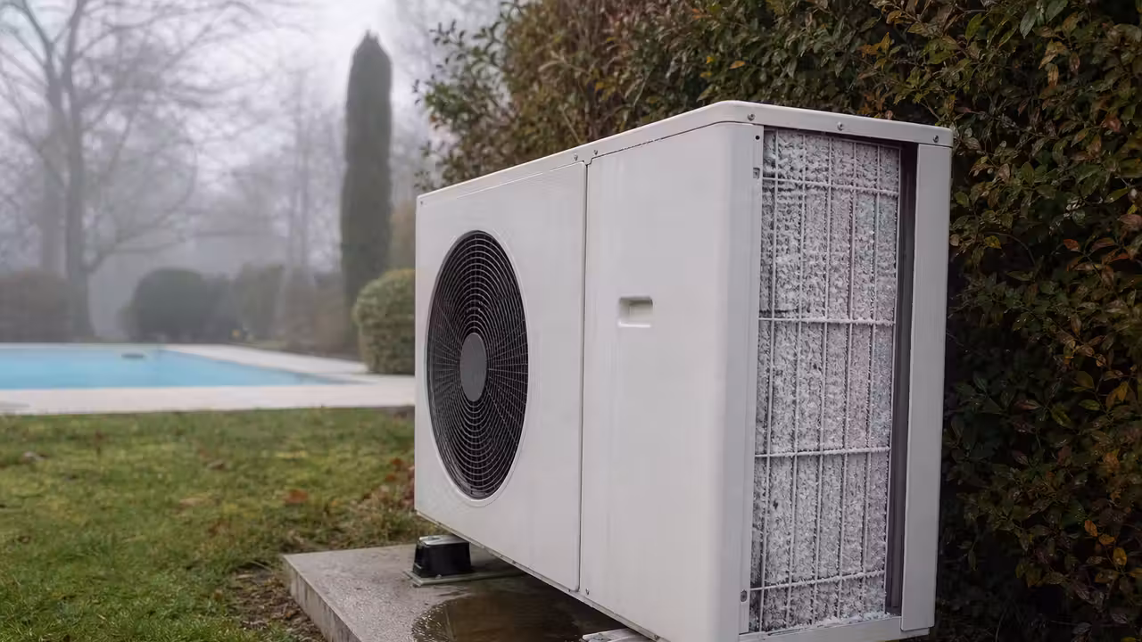 Pompe à chaleur de piscine sur une dalle au bord d'un bassin, ailettes de l'évaporateur couvertes de givre par temps de brume