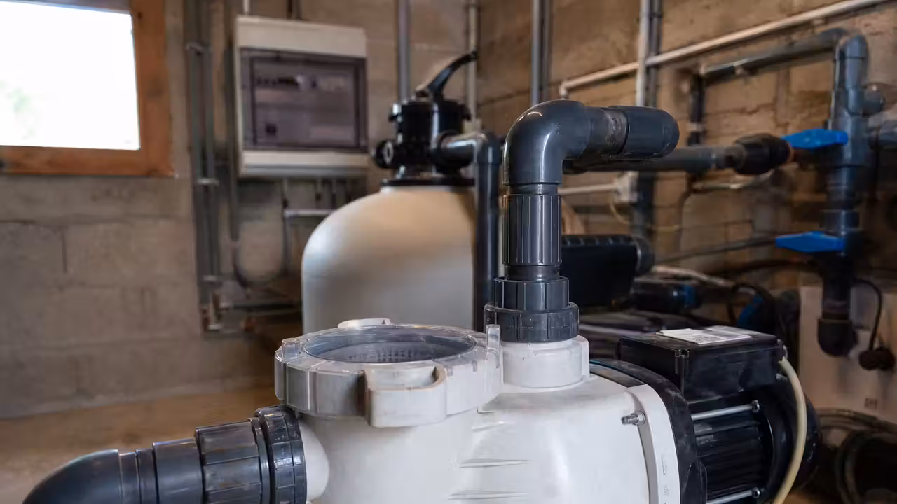 Pompe de filtration de piscine dans un local technique, corps de pompe et préfiltre transparent visibles