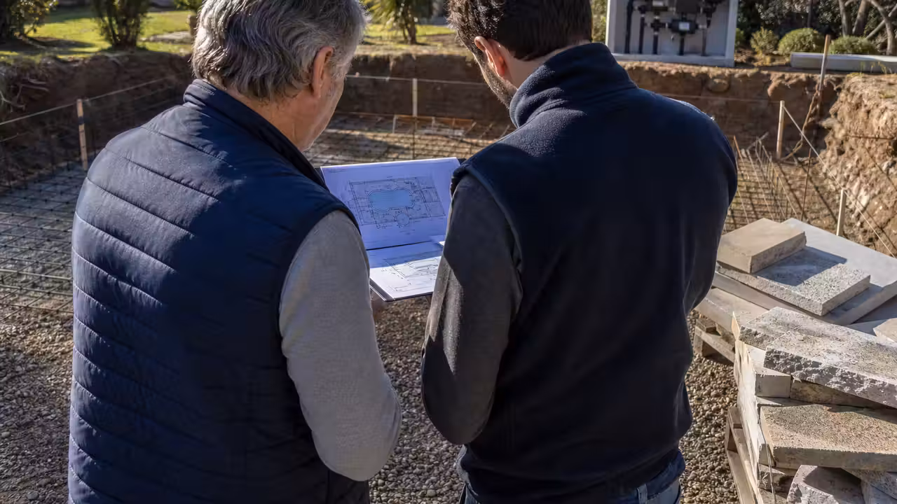 Professionnel et propriétaire comparant les plans et le devis d’une piscine près d’un chantier de terrassement