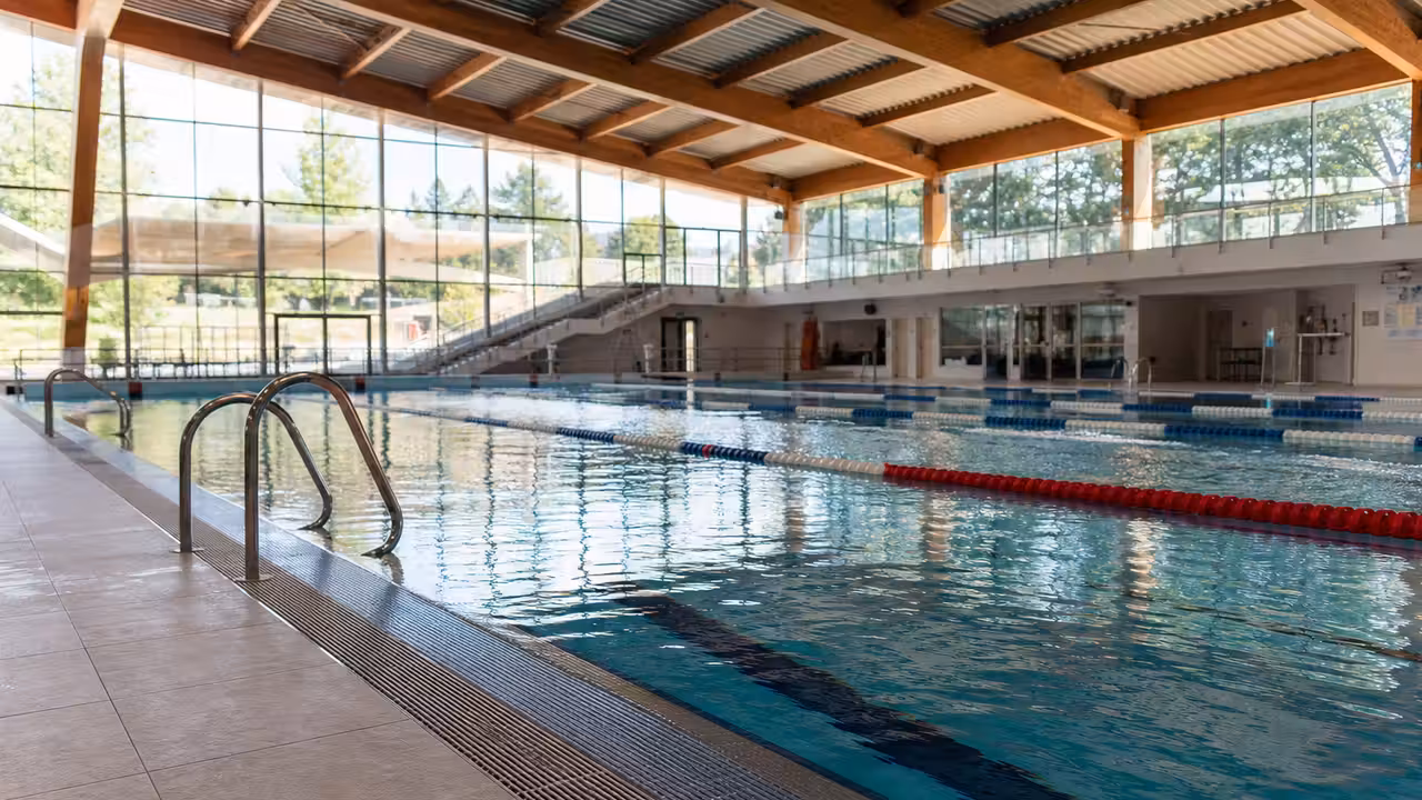 Bassin sportif intérieur à structure modulaire, lignes d’eau et plages carrelées sous lumière naturelle