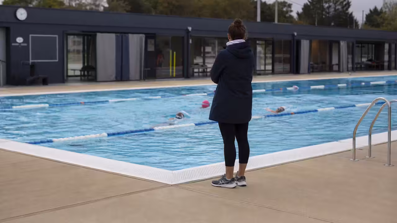 Bassin d’apprentissage de natation avec lignes d’eau et maître-nageur encadrant un groupe à distance