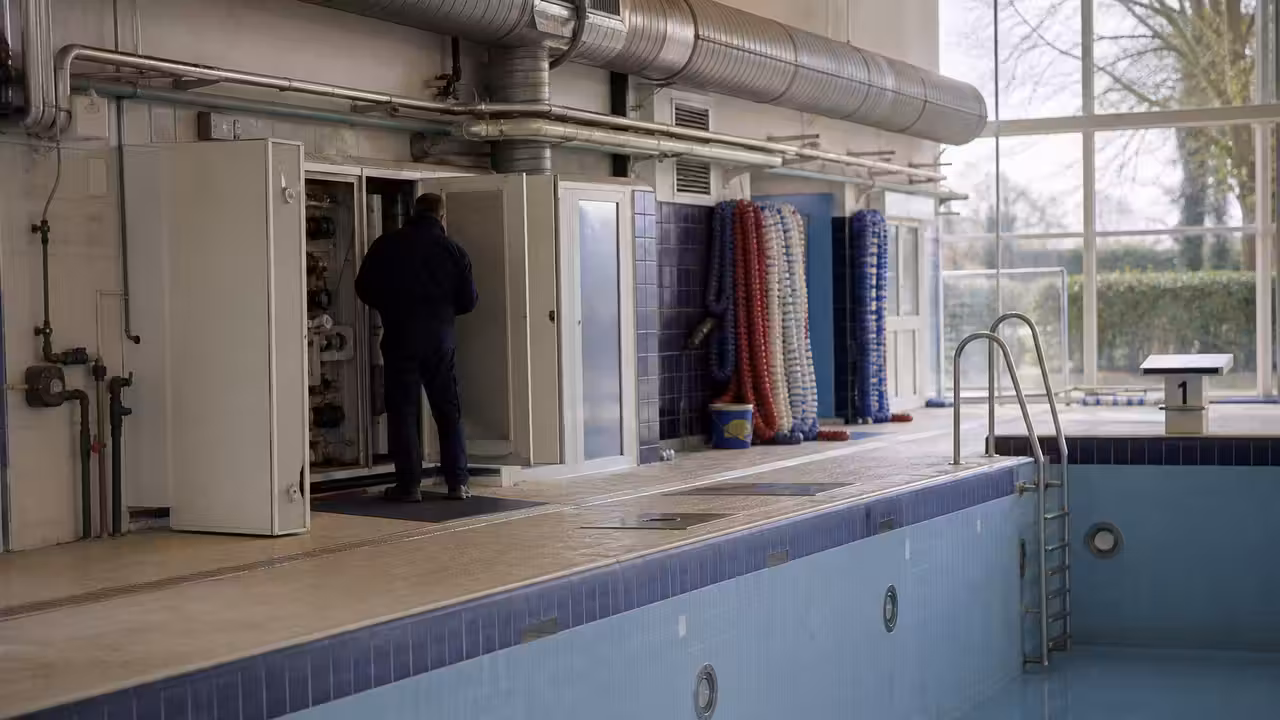 Bassin de piscine municipale vide pendant une période de maintenance hivernale, avec équipements techniques en arrière-plan