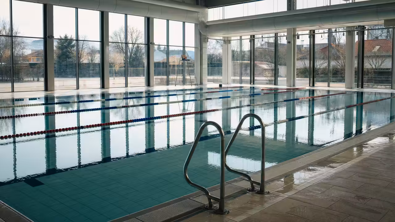 Bassin couvert de piscine publique avec baies vitrées, couloirs de nage et équipements de ventilation au plafond