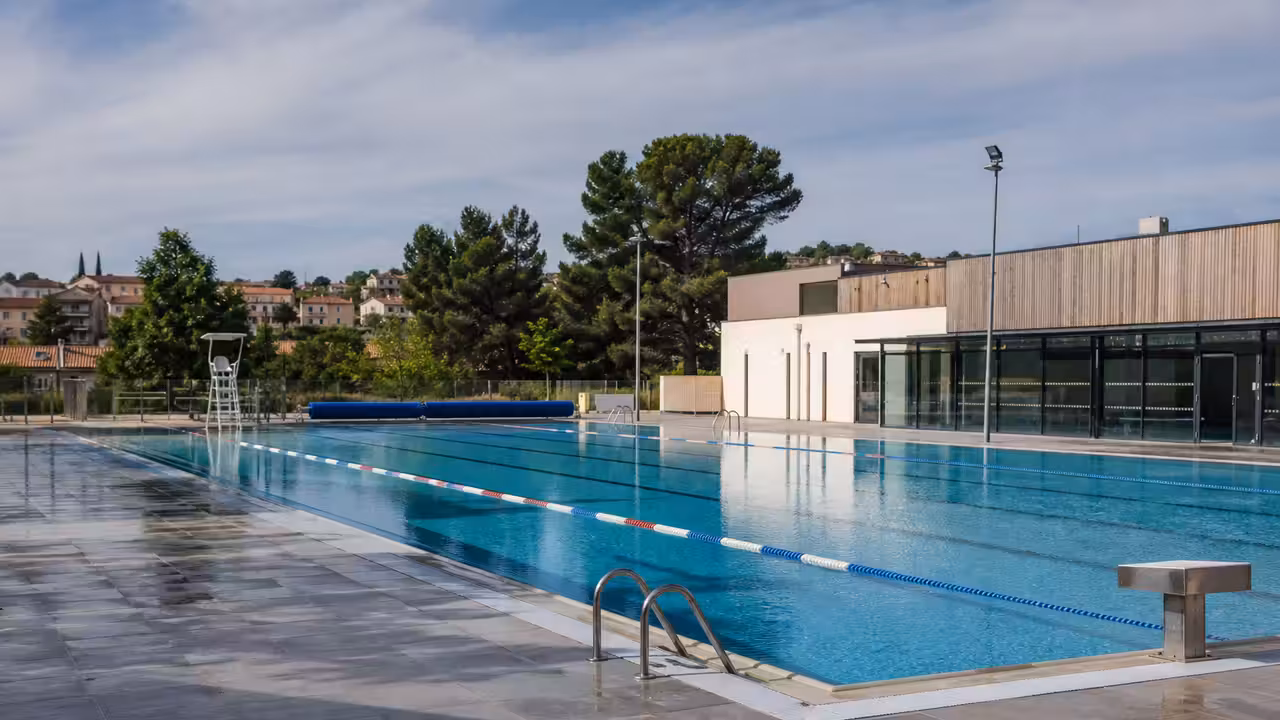 Bassin extérieur d’un centre aquatique municipal vide au petit matin, avec plages antidérapantes et ligne d’eau