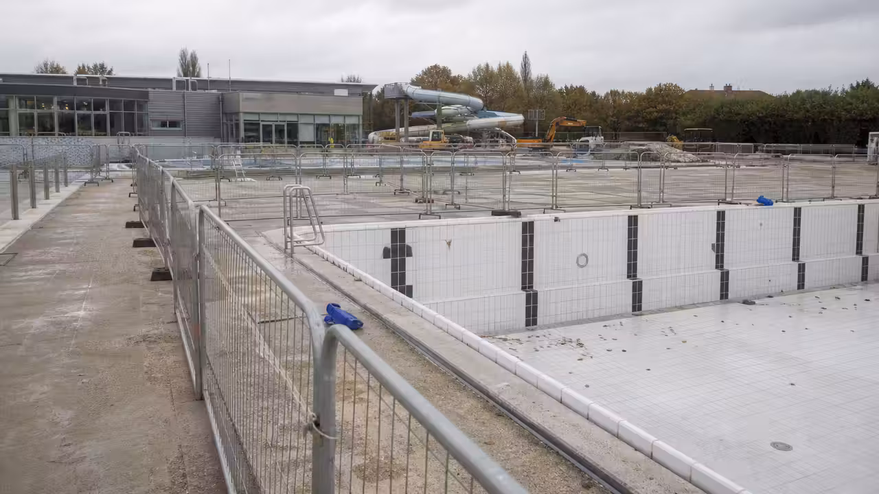 Site de piscine municipale en rénovation avec bassin vide et structures de chantier en arrière-plan