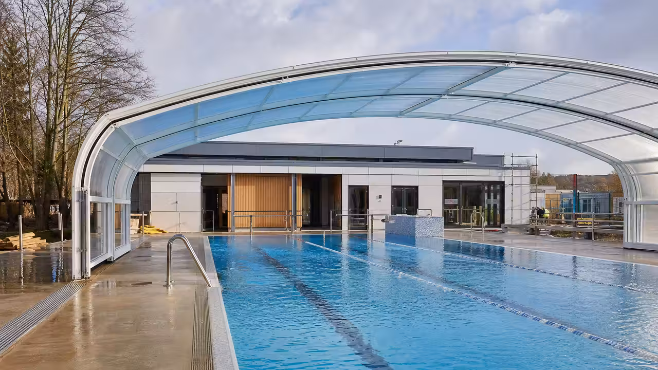 Bassin extérieur de piscine municipale avec couverture rétractable et vestiaires modernisés en arrière-plan