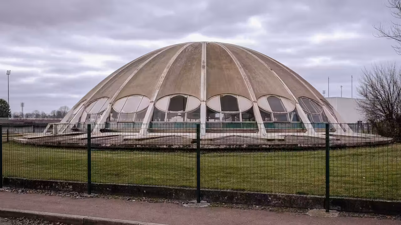 Le dôme circulaire d’une piscine Tournesol fermée, vu depuis l’extérieur derrière une clôture.