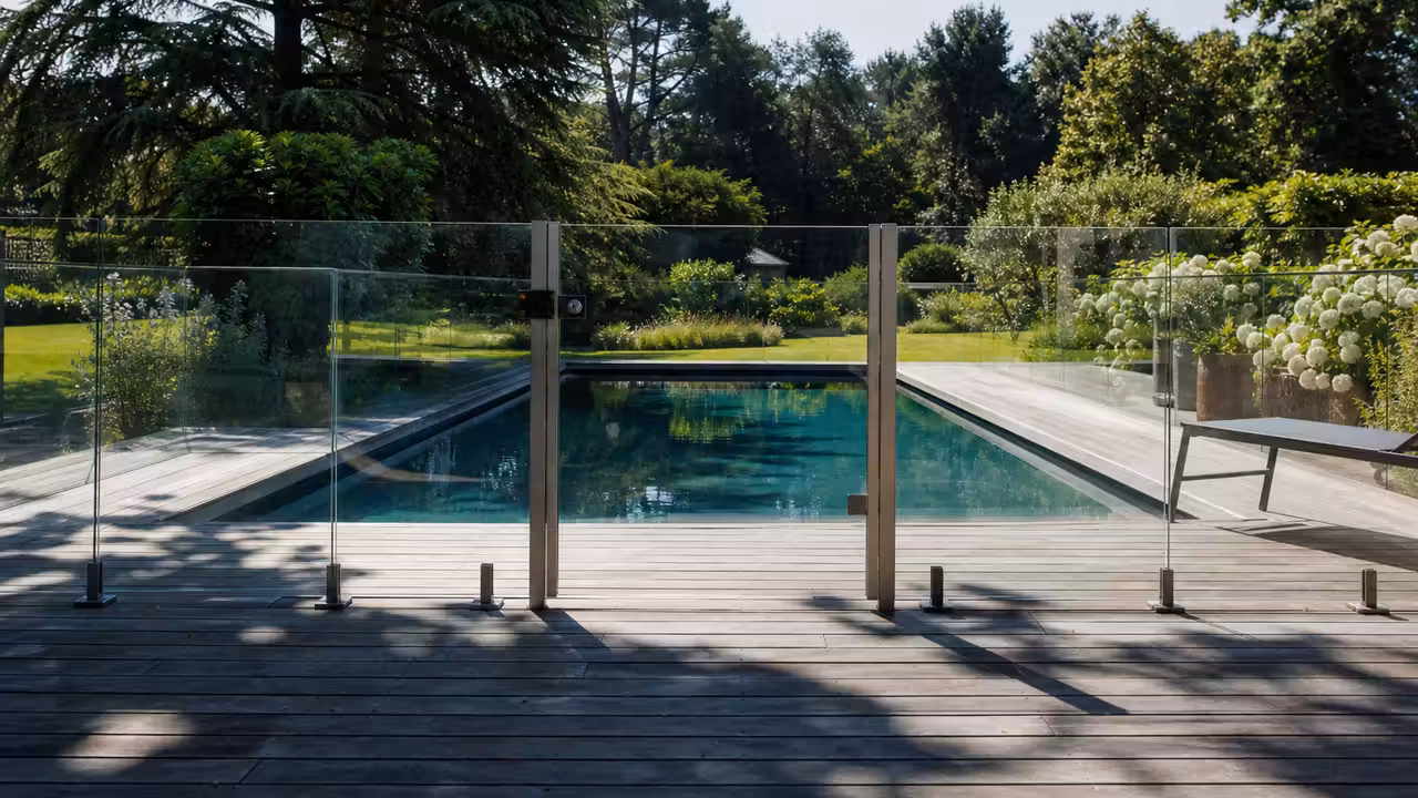 Barrière transparente verrouillée autour d’une piscine familiale enterrée sur une terrasse en bois
