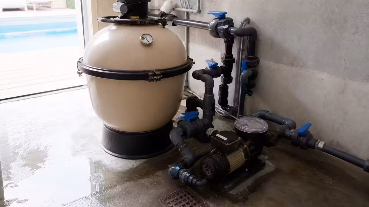 Équipement de filtration de piscine avec pompe, cuve à sable et manomètre dans un local technique propre