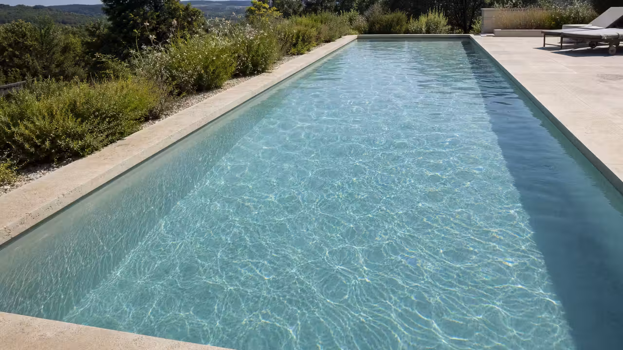 Piscine familiale rectangulaire à fond plat vue depuis la margelle, eau claire laissant deviner le fond clair du bassin