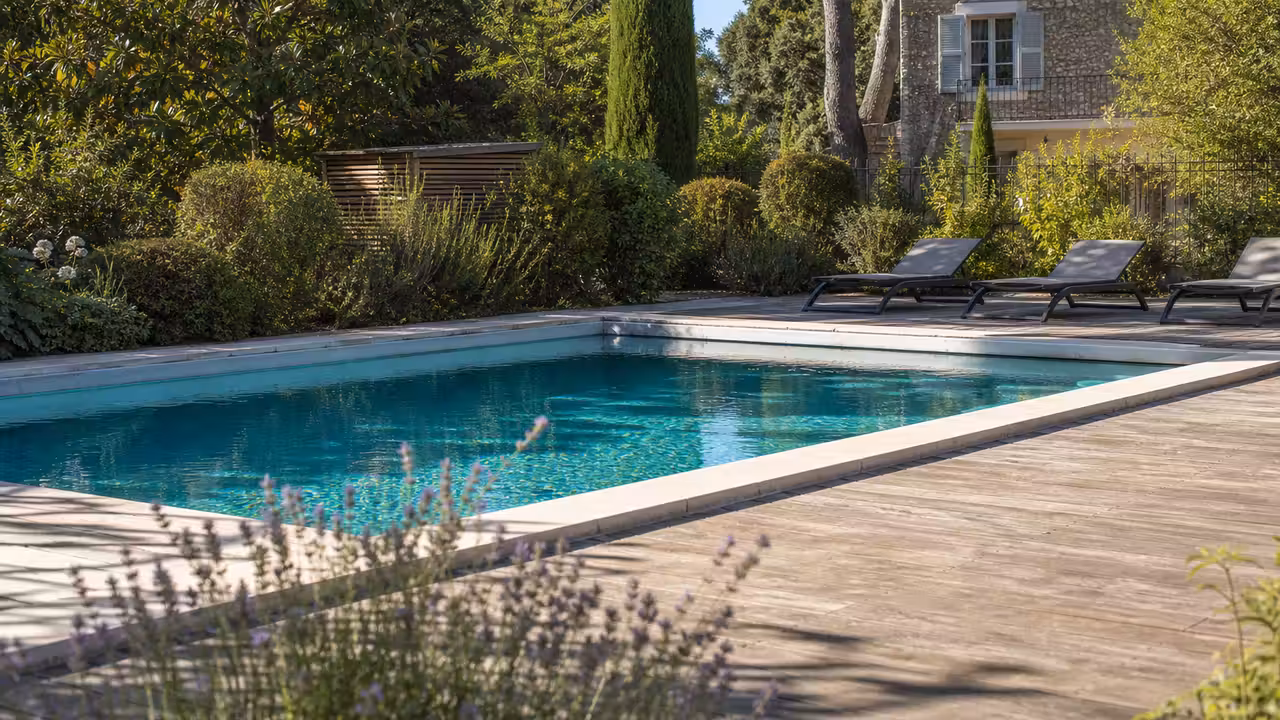 Piscine rectangulaire intégrée à une terrasse en bois dans un jardin arboré avec local technique discret