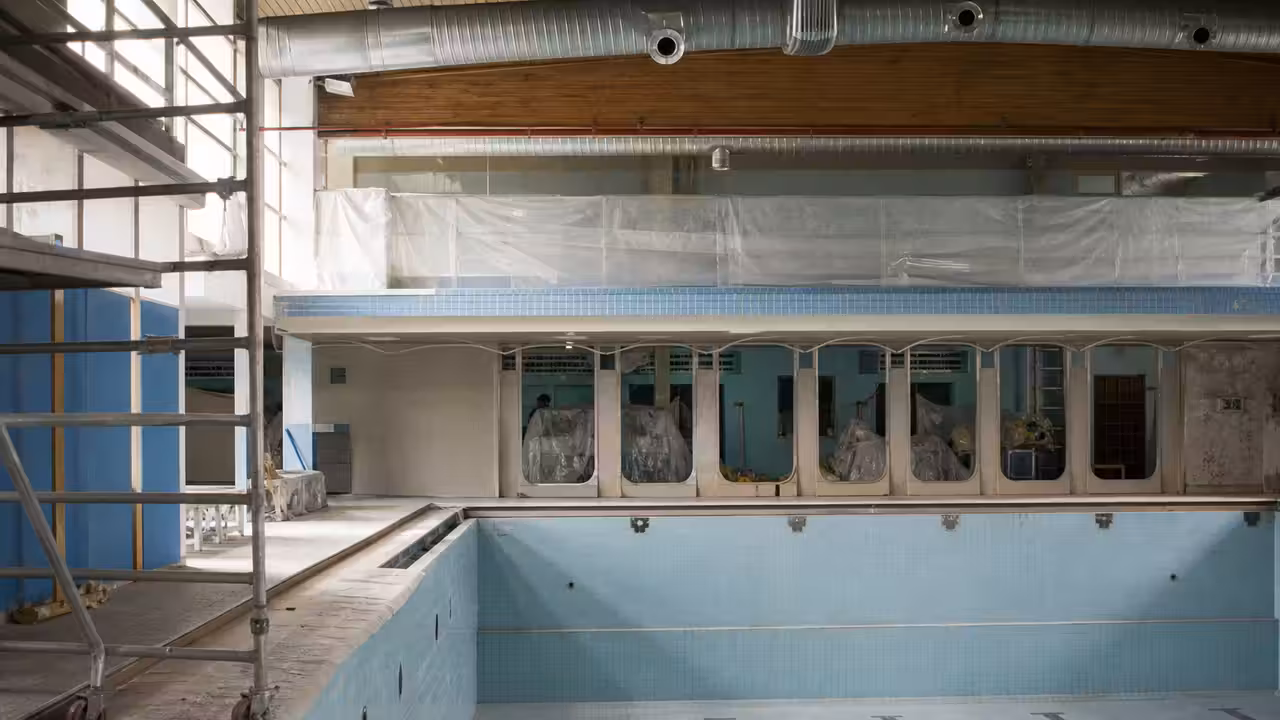 Halle de piscine municipale en rénovation, avec bassin vide, échafaudage et réseaux techniques apparents