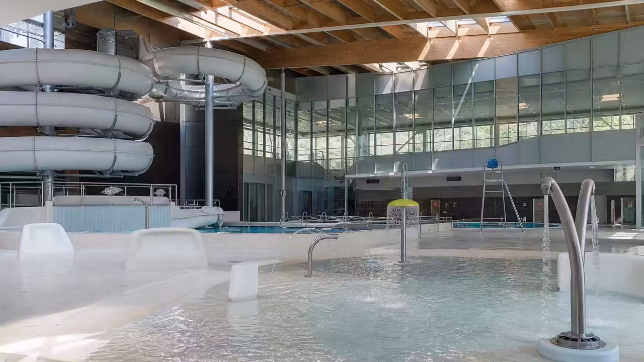 Vue intérieure d’un centre aquatique familial avec toboggan, jeux d’eau et bassins surveillés