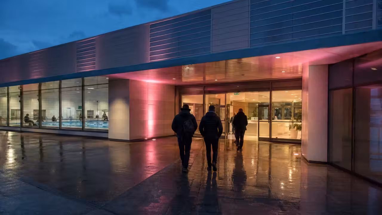 Entrée d’un centre aquatique éclairée en rose au crépuscule lors d’une campagne de sensibilisation