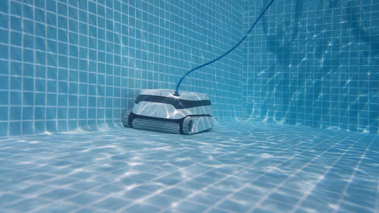 Robot nettoyeur de piscine électrique au fond d'un bassin, près d'un angle carrelé, avec son câble flottant à la surface