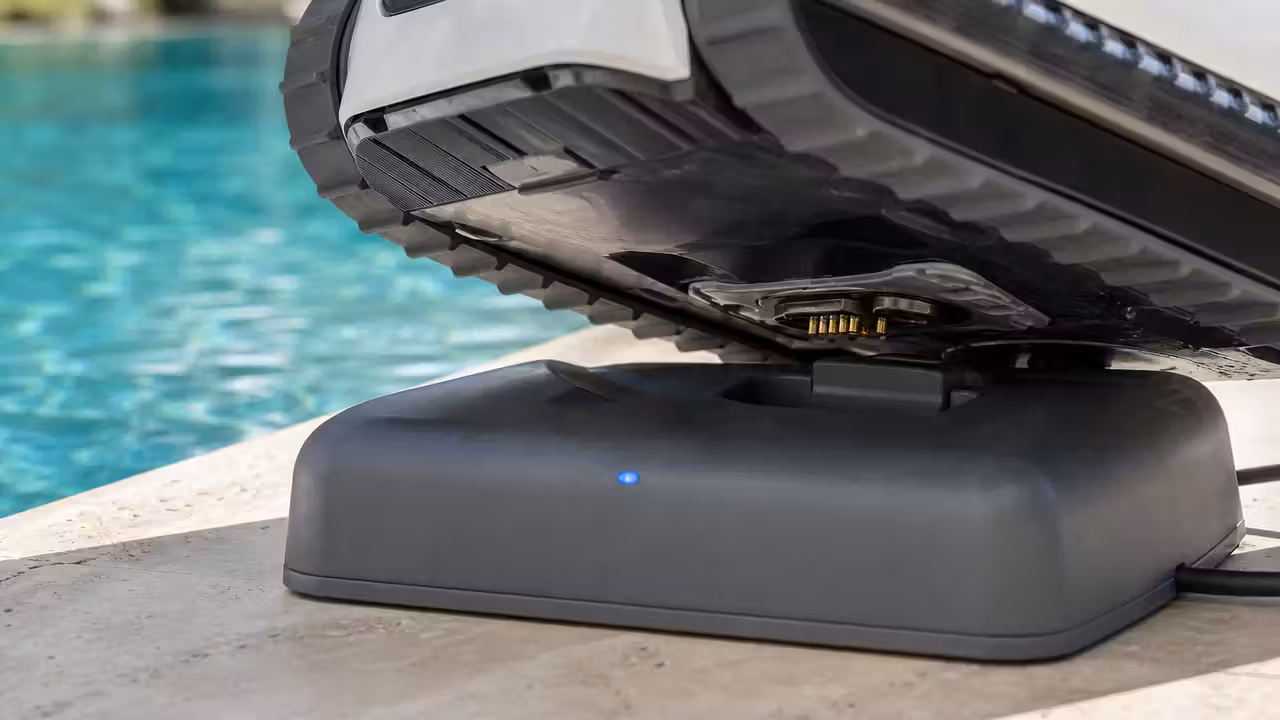 Robot de piscine sans fil posé sur sa station de charge au bord d'un bassin, contacts électriques visibles