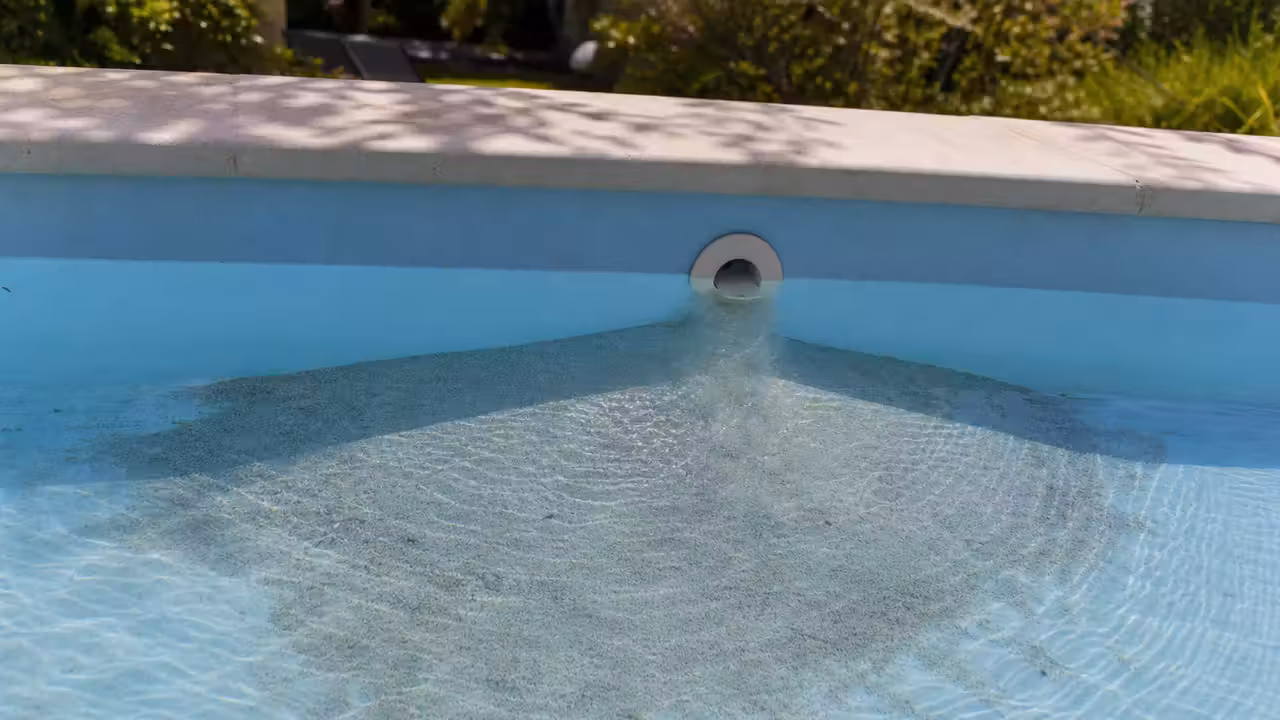 Fine couche de sable clair déposée au fond d'une piscine privée devant une buse de refoulement, eau limpide