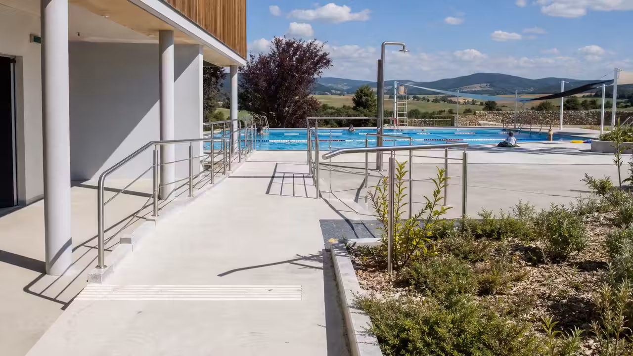 Entrée d’une piscine municipale récente avec bassin extérieur et espaces de circulation accessibles