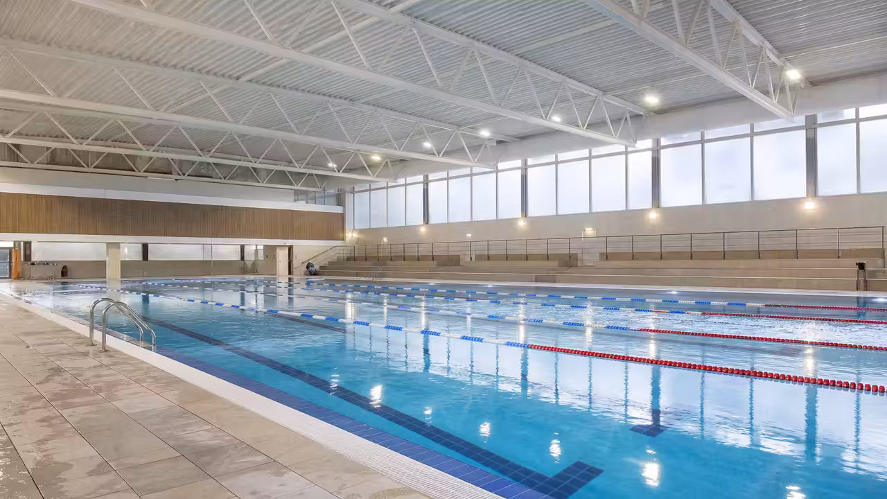 Grand bassin couvert rénové d'une piscine municipale, avec lignes d'eau, inox et lumière naturelle