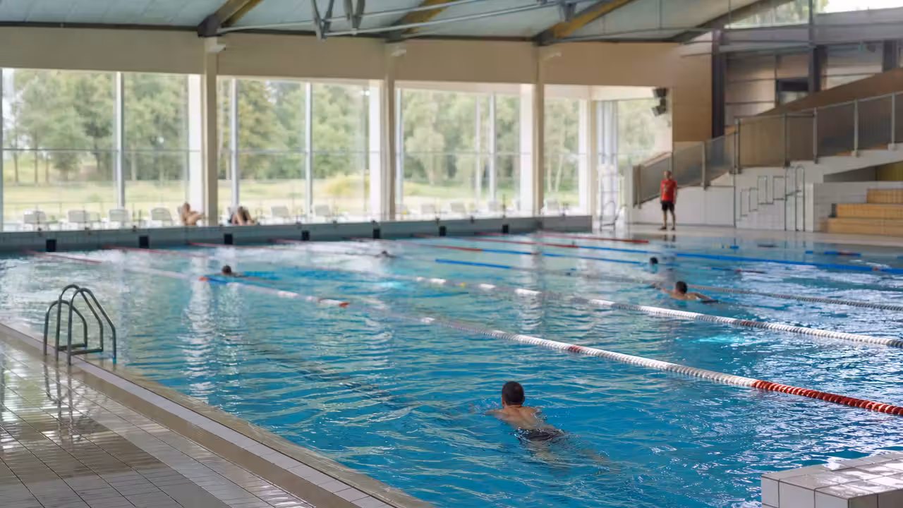 Bassin intérieur d’une piscine municipale avec lignes d’eau, maître-nageur au loin et usagers nageant