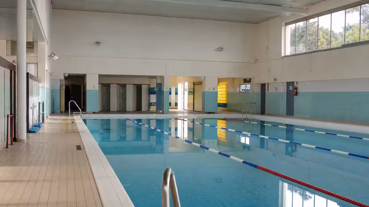 Bassin couvert d’une piscine municipale, lignes d’eau et baies vitrées éclairées par la lumière du jour.