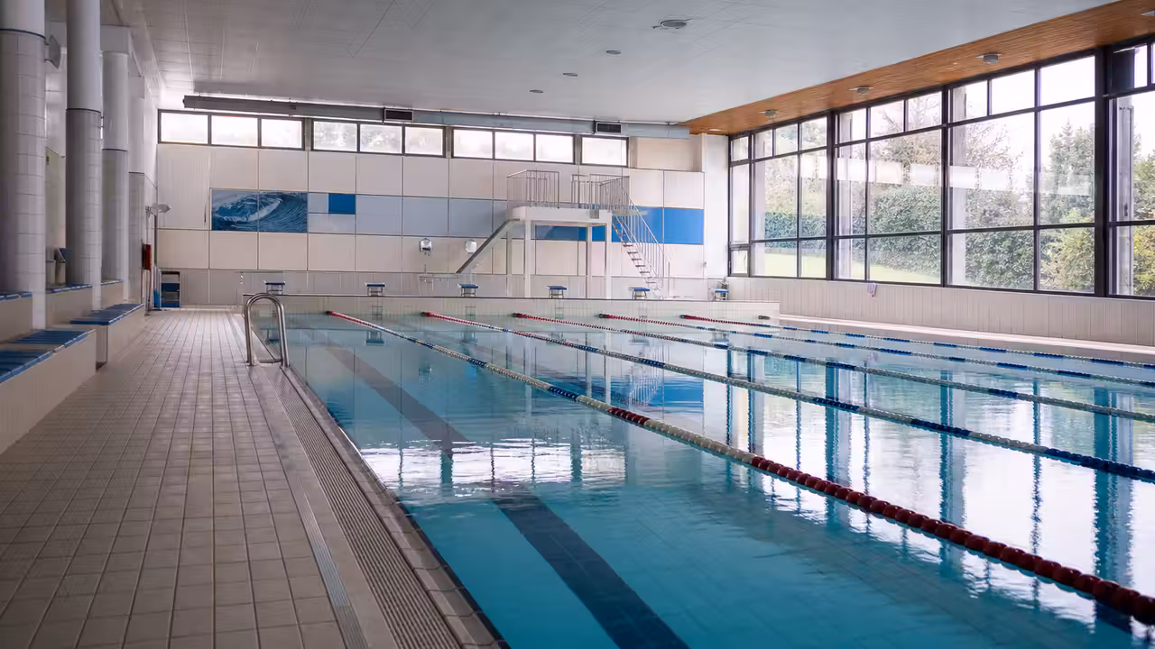 Bassin couvert d’une piscine publique avec lignes d’eau, gradins sobres et lumière naturelle latérale