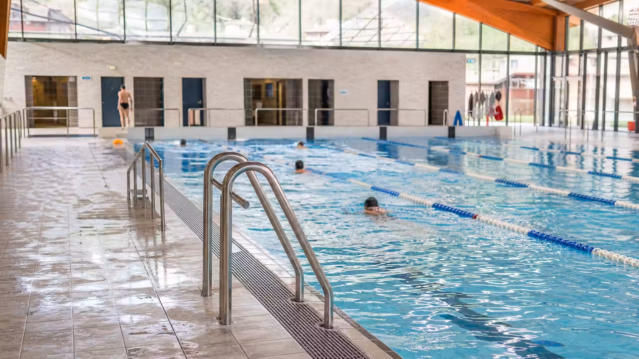 Bassin municipal lumineux avec lignes d’eau, vestiaires en arrière-plan et nageurs vus de dos