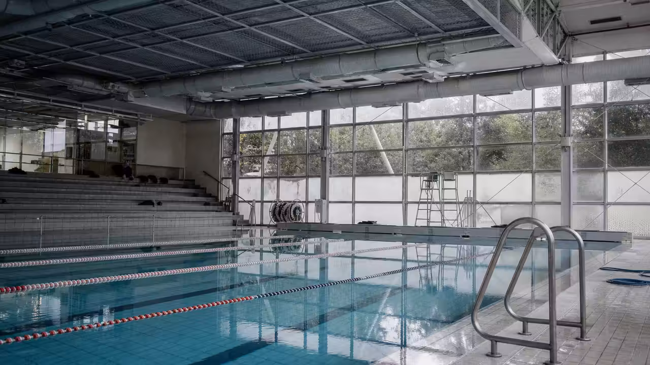 Bassin municipal couvert vide avec lignes d’eau, baies vitrées embuées et installation de ventilation au plafond